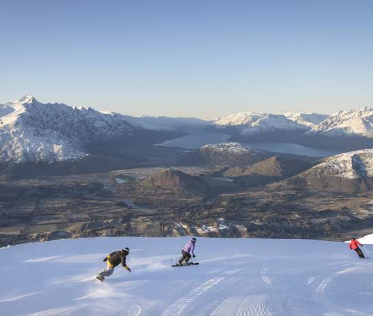 Three snowboarders riding down snowy mountain