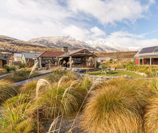 Exterior view of The Headwaters Eco Lodge, with native bush, rustic cabins and snowy mountains in the background