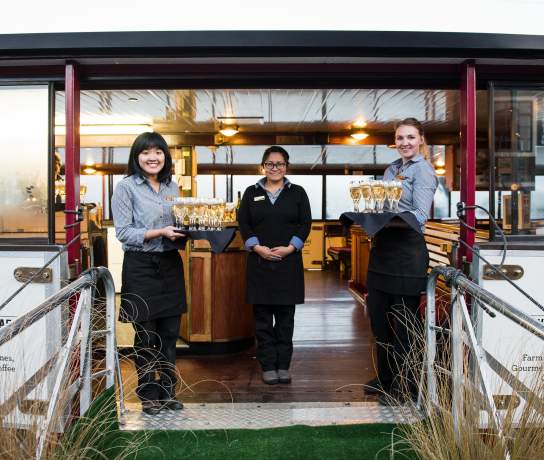 Waitresses waiting to greet guests onto a boat with trays of champagne