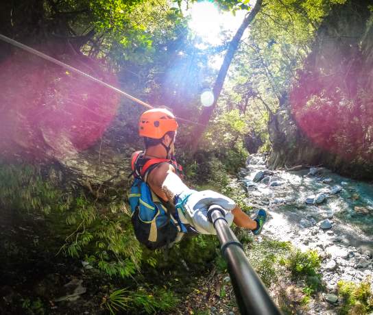 Person ziplining through a forest, over a river