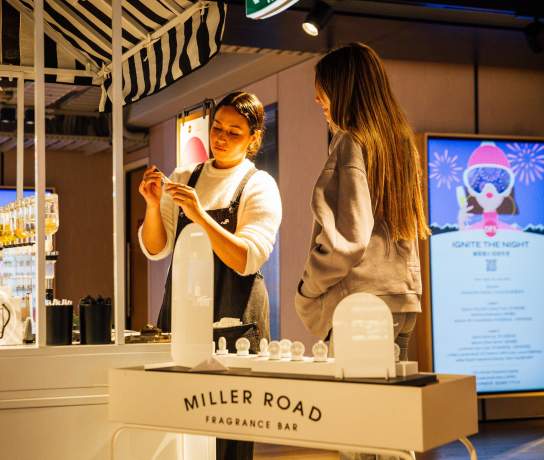 A white stand inside a shop with two girls making perfume