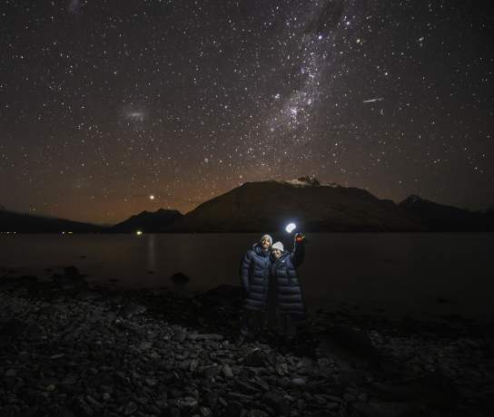 Two people holding a light with a background of mountains and a starry night sky