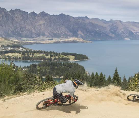 Person biking Queenstown Bike Park with view overlooking lake Whakatipu and the Remarkables mountain ranges