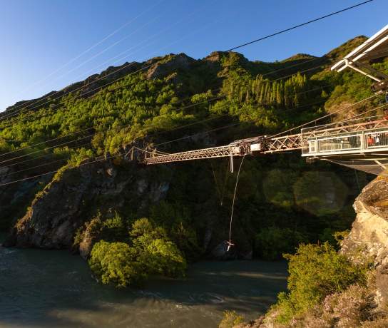 Wide shot of someone bungy jumping off a bridge over a river