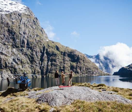 People having a picnic next to a high alpine lake with a helicopter next to them