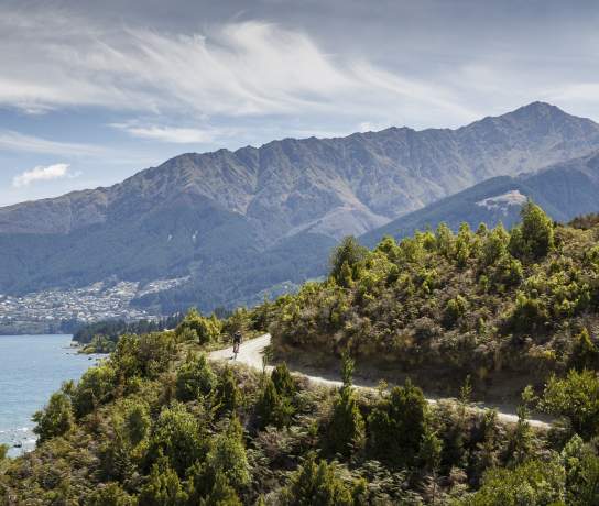 Person biking Jack's Point Trail, with Queenstown and Ben Lomond mountain in the background