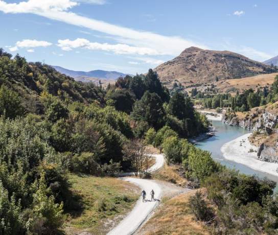Aerial view of the Shotover Gorge Trail,with two bikers cycling next to a blue river in a Canyon