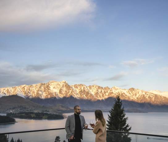 People enoying a wine on the balcony of Nest Kitchen and Bar overlooking the snow-covered Remarkables mountain range
