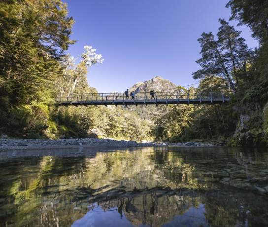 Ground of friends crossing a swing bridge on the Routeburn Track with a mountain in the background