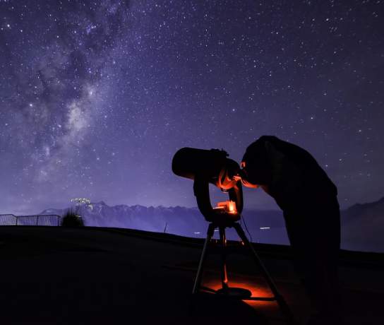 Person with telescope stargazing underneath the milky way near The Remarkables mountain range