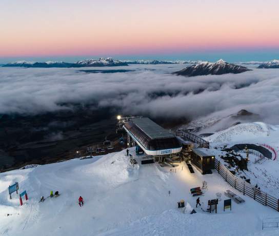 Soft warm hues of the sunrise at Coronet Peak with mountain poking out above clouds