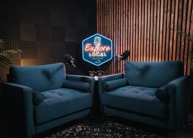 Explore Local podcast studio in Cedar City, featuring two chairs, microphones, and a glowing sign in a cozy recording space