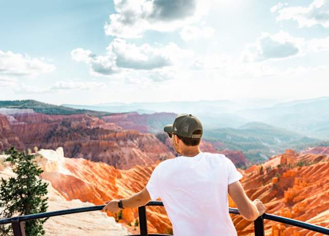 Person standing at scenic overlook at Cedar Breaks National Monument with a red rock canyon in the background and blue skies.