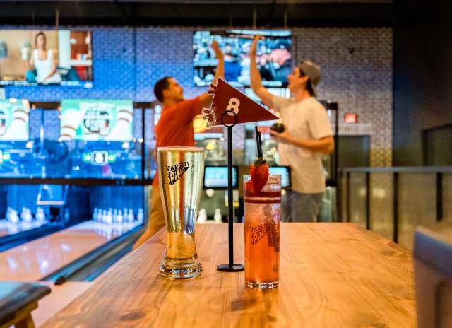 two guys high-fiving in a blowline alley with drinks in the foreground