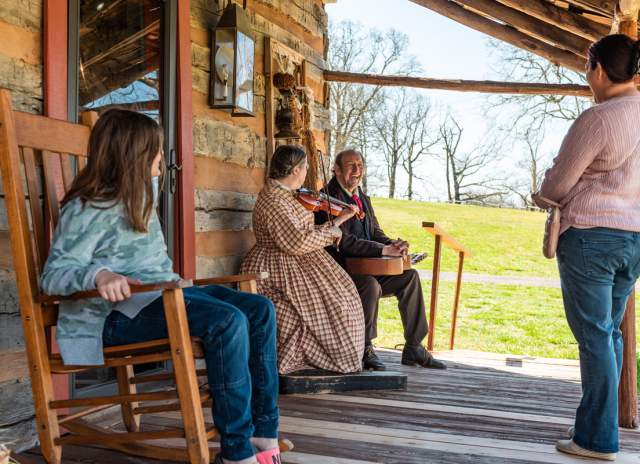 a young girl and woman enjoy music being played on the porch of a log cabin