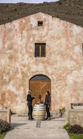 A person having a wine tasting outside Chard Farm Cellar door, a dusty pink Mediterranean style building