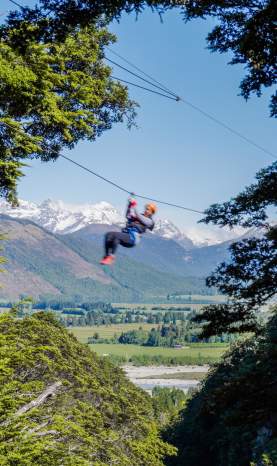 Person ziplining with snow-covered mountain in the back