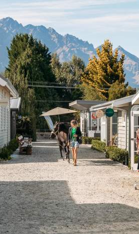 A lady walking a horse on a path lined with boutique cabins and shops