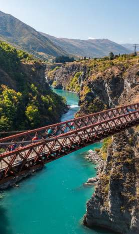 People biking over a bridge with vibrant blue water below