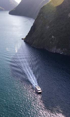 Aerial view looking down a boat cruising in a fiord surrounded by towering peaks