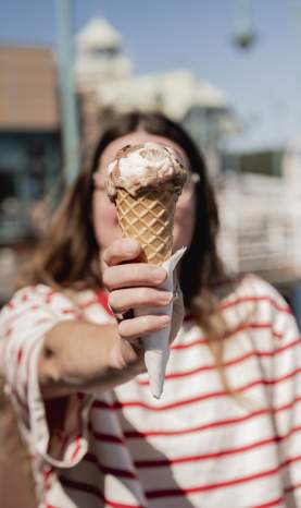 A woman holding a chocolate vanilla ice cream cone to the camera