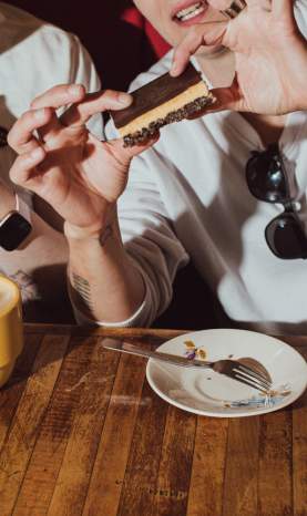 Two people eating Nanaimo bars with a latte.