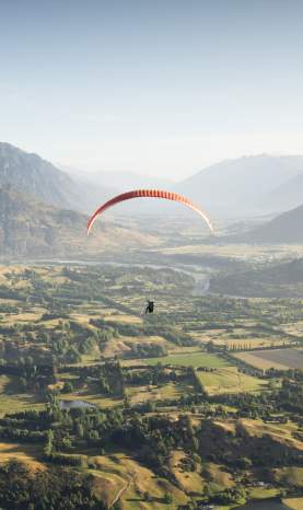 Person paragliding with a green valley, dramatic view of the Remarkables mountain in the background