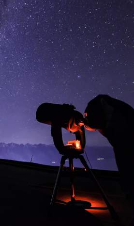 Person with telescope stargazing underneath the milky way near The Remarkables mountain range