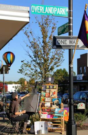 An artist sits at their art fair station painting on a canvas and selling their art
