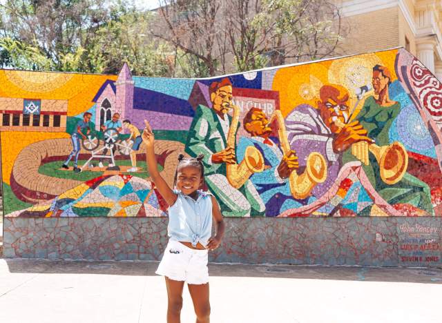 Child strikes a pose in front of the Rhapsody mosaic in East Austin depicting Austin's Black musical heritage