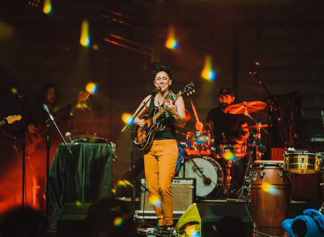 Gina Chavez on large stage with instruments in the background.