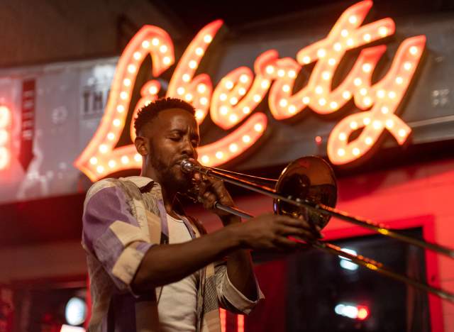 Austin musician Daniel Fears plays the trombone in front of The Liberty bar's lighted sign