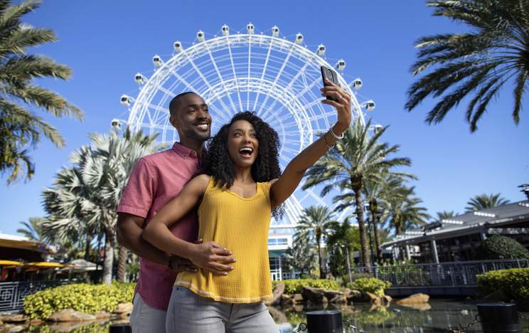 A couple posing for a selfie in front of The Wheel at ICON Park