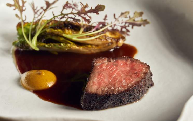 Perfectly seared Wagyu beef with charred greens, rich sauce, and a dollop of mustard, elegantly plated at ÔMO by Jônt.