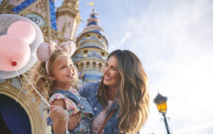 Mother and daughter holding a balloon in front of the castle at Magic Kingdom® Park