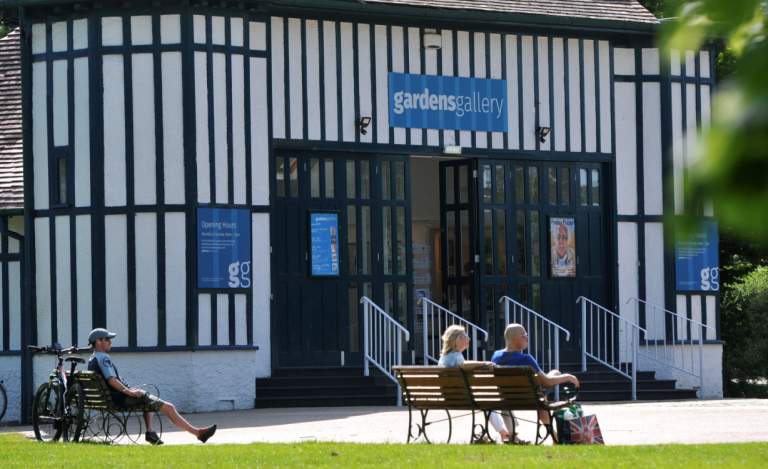 People sat on benches in front of the Gardens Gallery Cheltenham in Montpellier Gardens, Cheltenham.