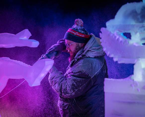 An ice sculptor using a power tool to carve a block of ice at the Freezefest ice battle