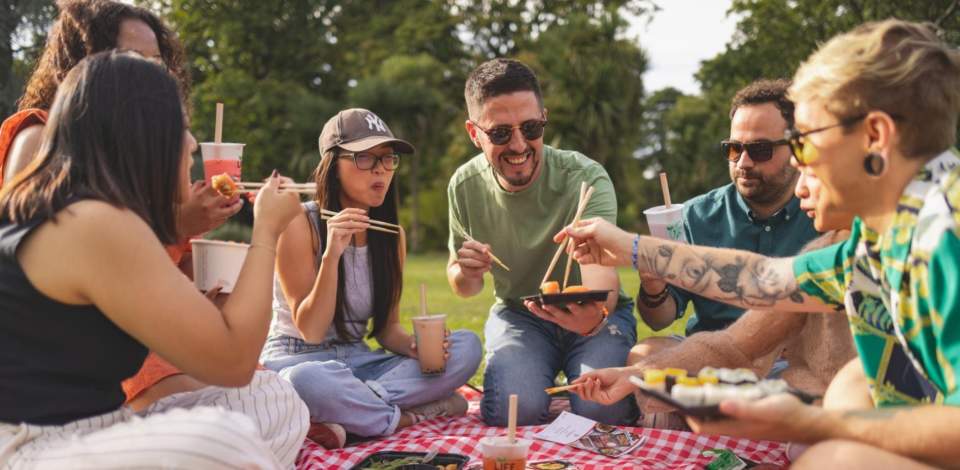 Group of friends enjoying sushi and bubble tea on a picnic blanket in the park