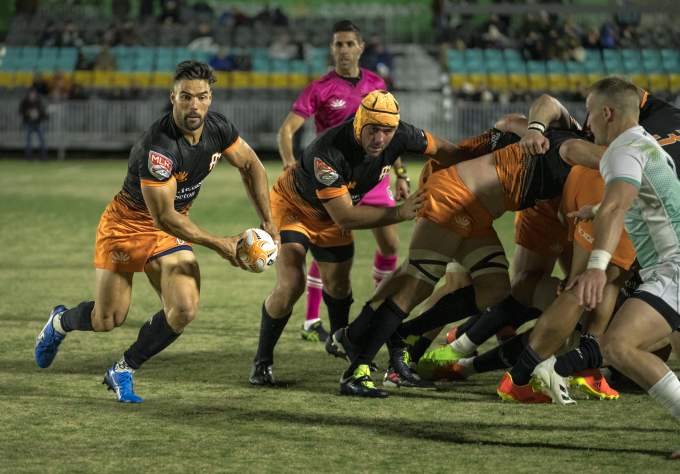 Austin rugby team, Austin Gilgronis, battling an opposing team while a player runs the ball towards the try zone.