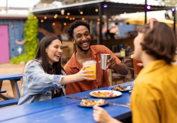 Two women and a man cheering drinks over plates of tacos.