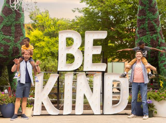 Family laughing in front of Be Kind sign at Elsewhere Garden Bar & Kitchen