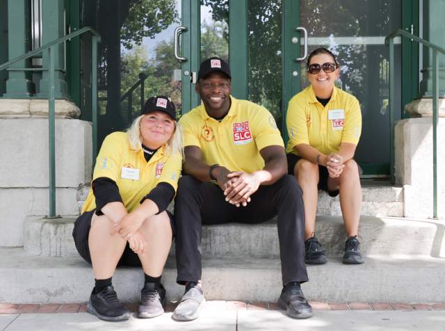 Three people sitting on steps wearing yellow downtown ambassadors shirts