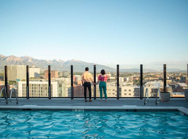 View of downtown Salt Lake looking across a pool with 2 people standing near the edge overlooking the city