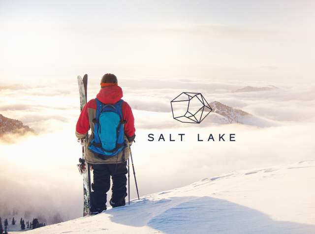 A skier holding skis looking out over a valley filled with clouds with Salt Lake and West of Conventional written on it.