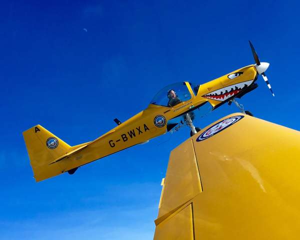 a yellow stunt aeroplane in the sky with a face painted on the nose