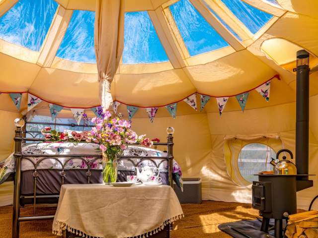 A glamping pod with woodburner and bed surrounded by flowers and bunting