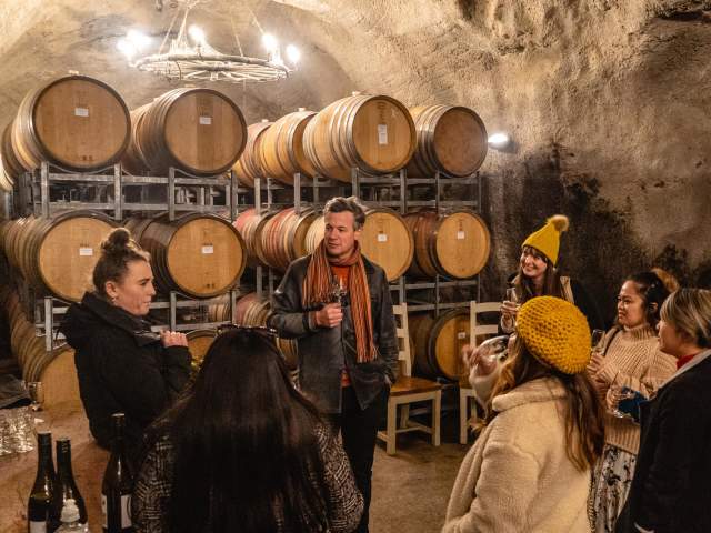 Group of people on a wine tour in an underground wine cave with wine barrels around