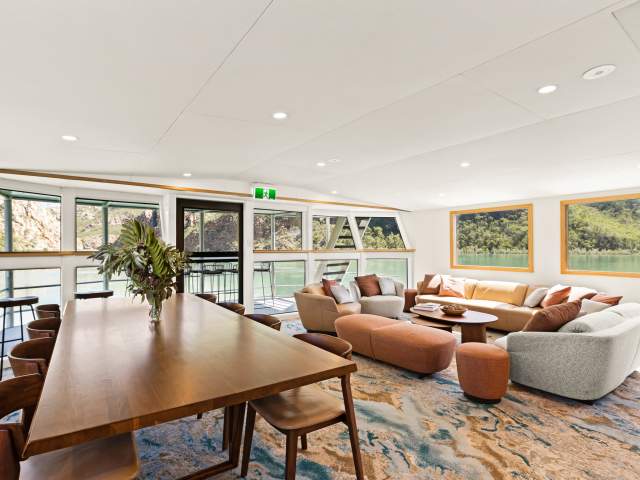 Lounge area of the Jetwave Pearl at the Horizontal Falls, showing comfortable lounge seating, dining table and chairs and views through the windows and balcony area
