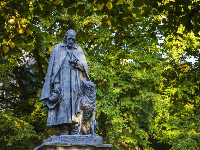 a statue of Alfred, Lord Tennyson with trees and green leaves in background