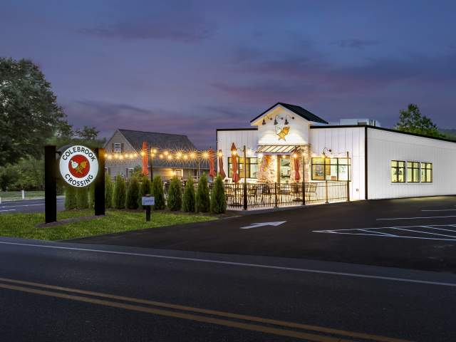 Exterior of an ice cream shop at night with string lights out front and a circular sign that reads Colebrook Crossing